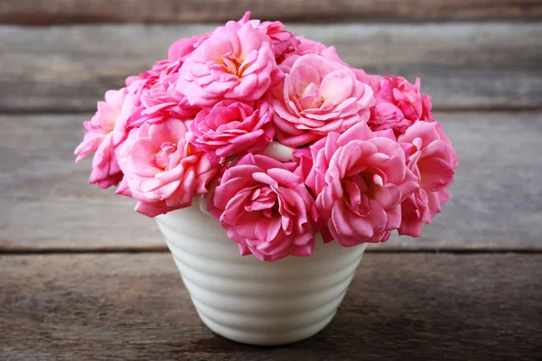 Красиві рожеві троянди в горщику на дерев'яному фоні — стокове фото