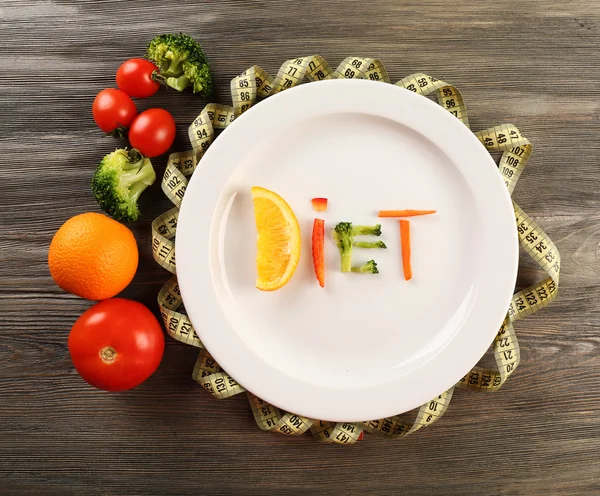 Word DIET made of sliced vegetables in plate with measuring tape on wooden table, top view — Stock Photo, Image