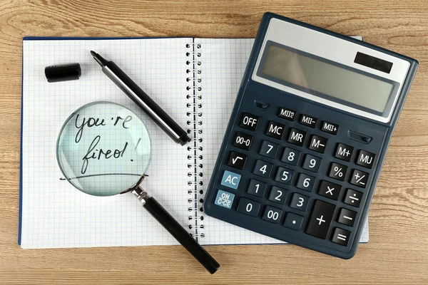 Meddelandet du är avskedad på anteckningsboken med miniräknare, markör och förstoringsglas på träbord, närbild — Stockfoto