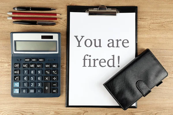 Message You 're Fired on clipboard on wooden table, top view — стоковое фото