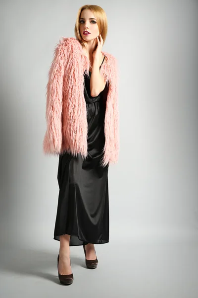 Modelo jovem expressivo em casaco de pele rosa e vestido preto no fundo cinza — Fotografia de Stock