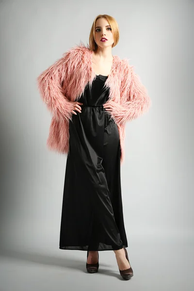 Expressive young model in pink fur coat and black dress on gray background — Stock Photo, Image