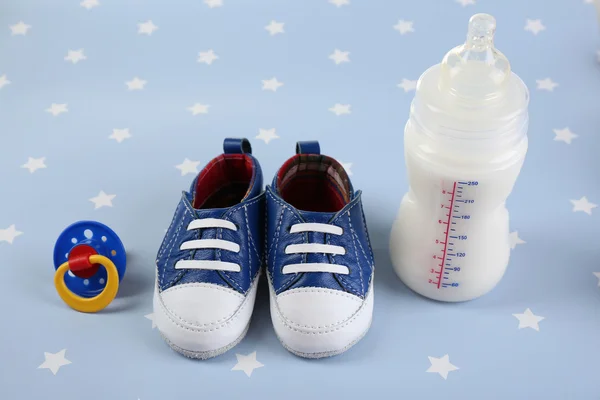 Chaussures bébé avec mamelon et biberon de lait sur fond bleu — Photo