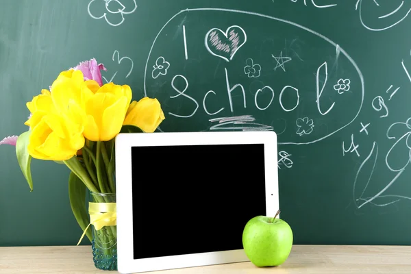 Digital tablet and apple on  desk in front of blackboard — Stock Photo, Image