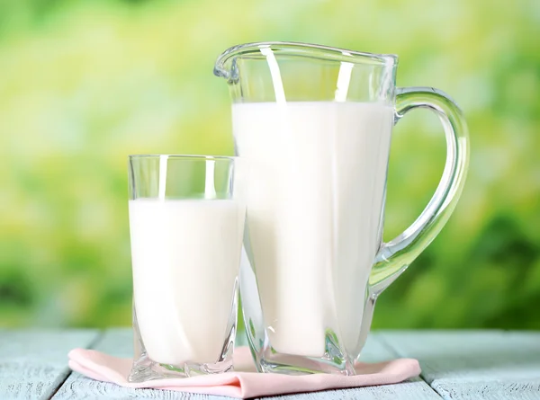 Pitcher and glass of milk on wooden table on natural background — Stock Photo, Image