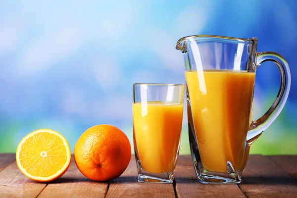 Szkło i dzban soku pomarańczowego na drewnianym stole na naturalne tło — Zdjęcie stockowe