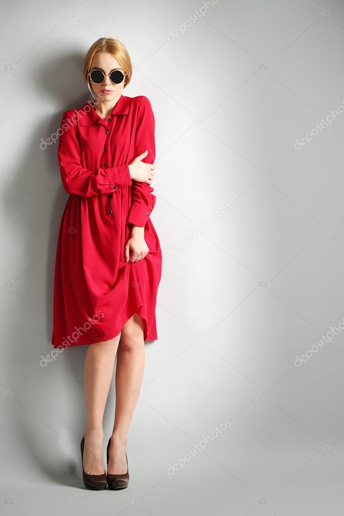 Expressive young model in red dress and sunglasses on gray background