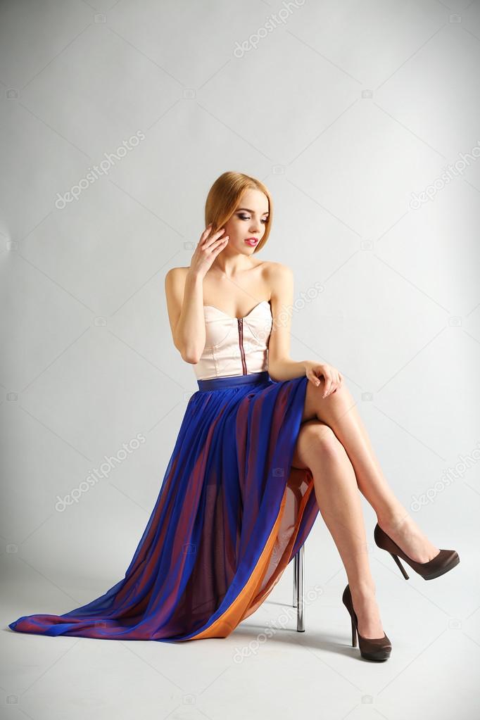 Expressive young model sitting on chair on gray background