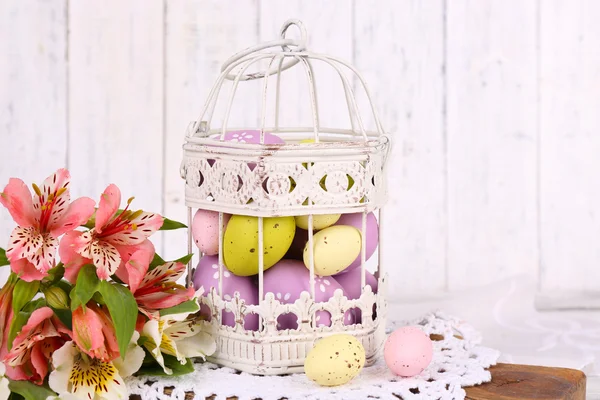 Пасхальные яйца в декоративной клетке и цветах — стоковое фото
