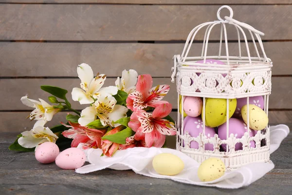 Huevos de Pascua en jaula decorativa y flores — Foto de Stock