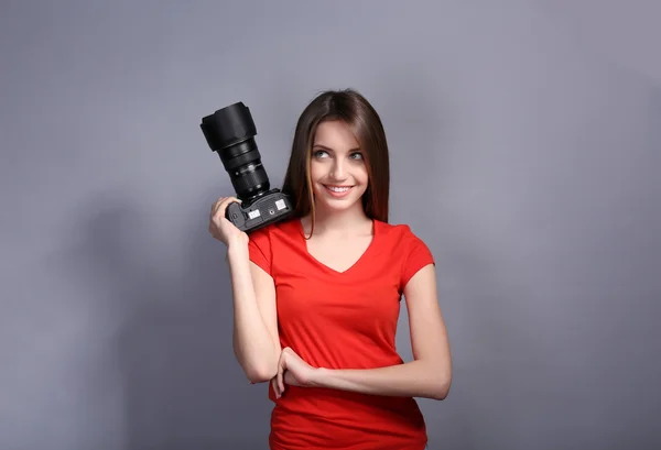 Young female photographer taking photos on grey background — Stock Photo, Image