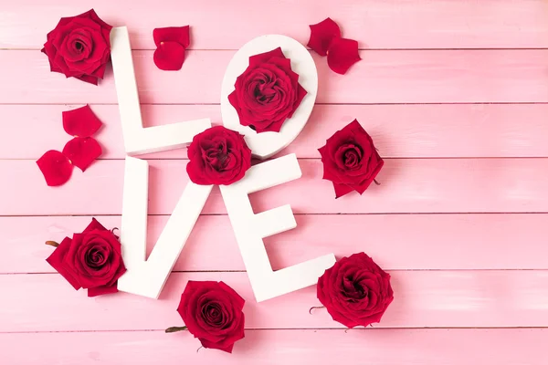 Schöne Rosen mit Wort Liebe auf rosa Holzplanken Hintergrund — Stockfoto