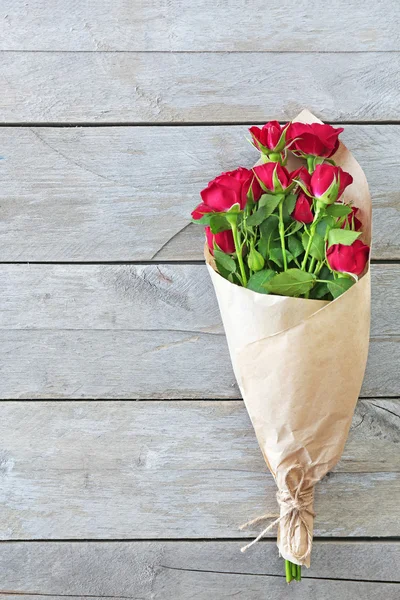 ดอกกุหลาบสีแดงห่อในกระดาษบนพื้นหลังโต๊ะไม้ — ภาพถ่ายสต็อก