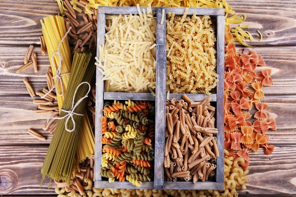Різні види макаронних виробів в коробці на дерев'яному фоні — стокове фото
