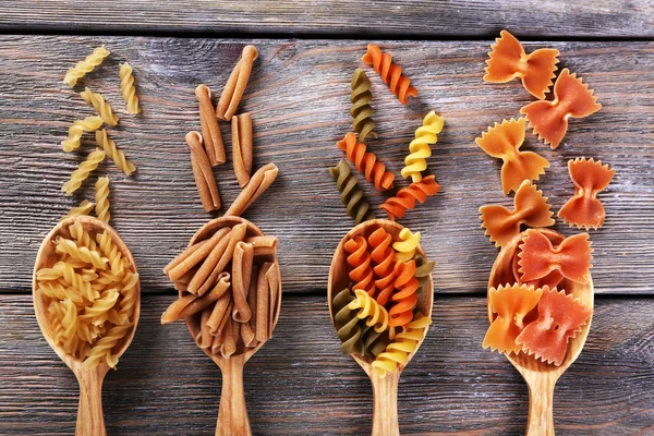 Different types of pasta in spoons on wooden background — Stock Photo, Image