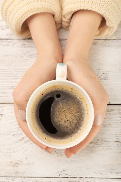 Manos femeninas sosteniendo taza de café sobre fondo de madera — Foto de Stock