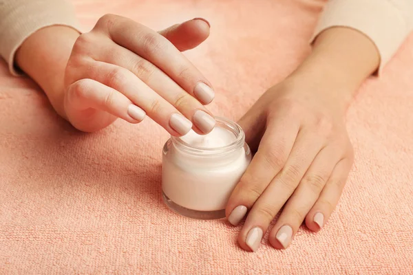 Manos femeninas con tarro de crema sobre fondo de tela — Foto de Stock