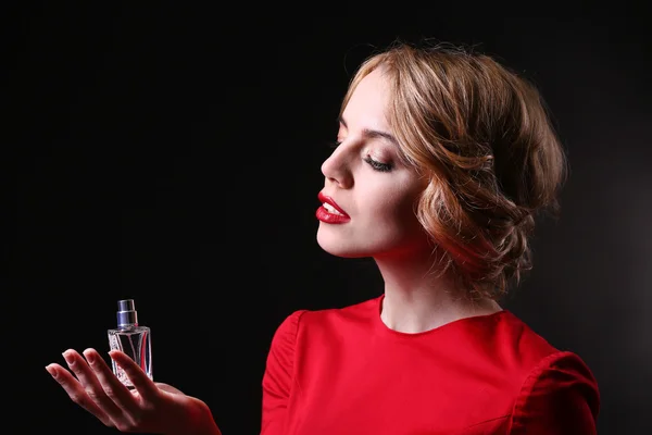 Hermosa joven con botella de perfume sobre fondo negro — Foto de Stock