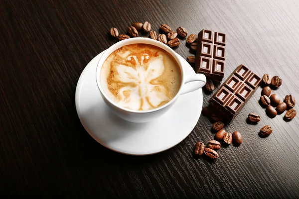 Cup of latte art coffee with grains and bar of chocolate on wooden background — Stock Photo, Image