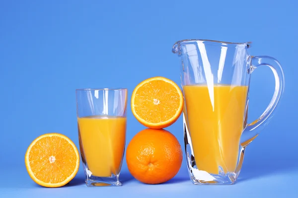 Vidro e jarro de suco de laranja no fundo azul — Fotografia de Stock