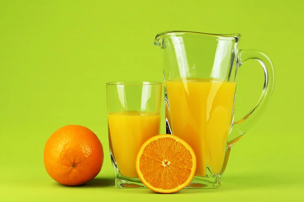 Glass and pitcher of orange juice on green background — Stock Photo, Image