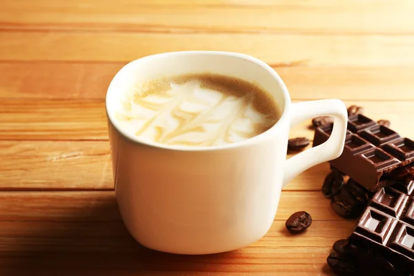 Xícara de café arte latte com grãos e chocolate sobre fundo de madeira — Fotografia de Stock