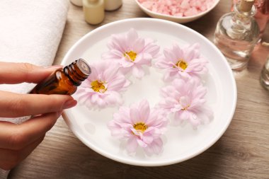 Kadın el özü şişe ve spa su ahşap masaya, closeup çiçek ile kase