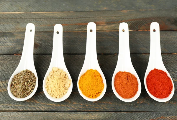 Different kinds of spices in spoons on wooden background — Stock Photo, Image