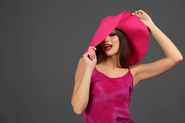 Hermosa mujer joven en vestido rosa y sombrero sobre fondo gris oscuro —  Fotos de Stock