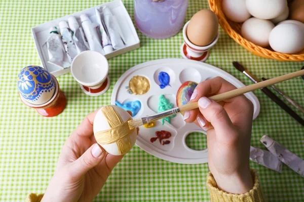 Pintura de huevos de Pascua por manos femeninas sobre fondo de mantel colorido — Foto de Stock