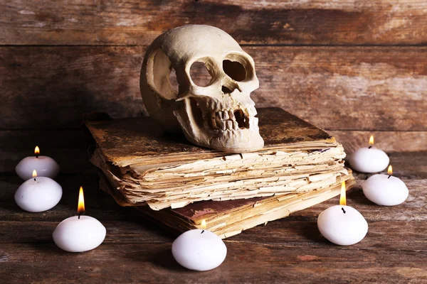人間の頭蓋骨、レトロな本と木製のテーブル、クローズ アップでろうそくの明かりのある静物 — ストック写真