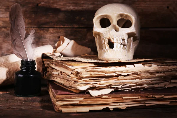 人間の頭蓋骨、レトロな本と木製のテーブル、クローズ アップのクイルのある静物 — ストック写真