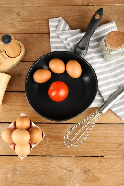 Still life with eggs and pan on wooden table, top view — Stock Photo, Image