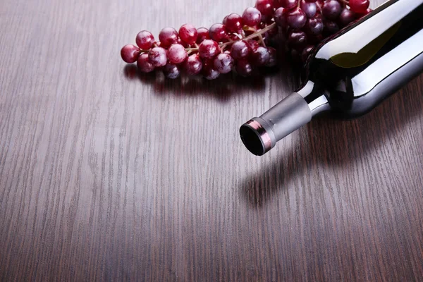 Láhev červeného vína s hroznovým vínem na dřevěné pozadí — Stock fotografie