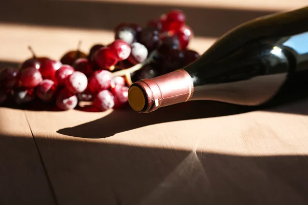 木製の背景にぶどうと赤ワインのボトル — ストック写真