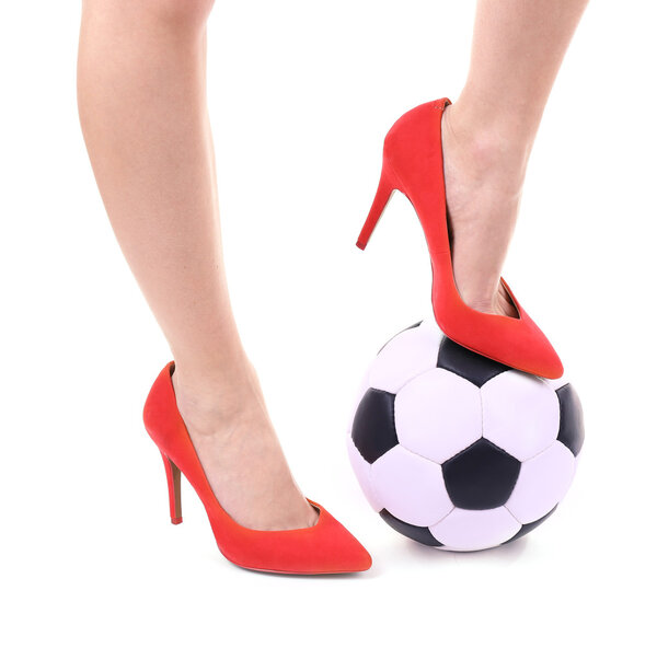 Женские ноги в красных туфлях на высоких каблуках с футбольным мячом, изолированным на белом
