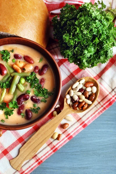 Bohnensuppe in Schüssel mit frischem Scheibenbrot auf Serviette, auf Holztischhintergrund — Stockfoto