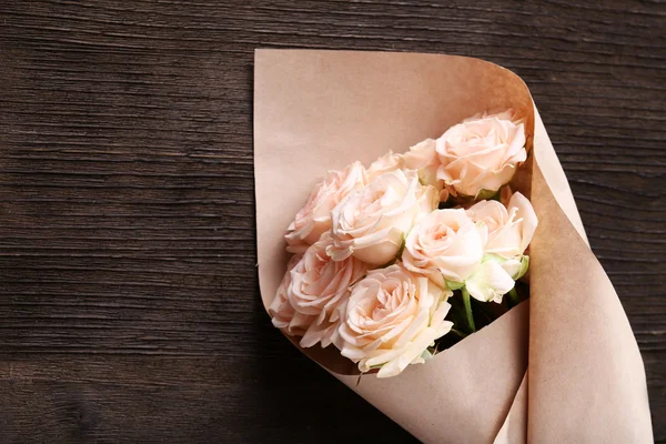 Букет красивых свежих роз, завернутых в бумагу на деревянном фоне — стоковое фото