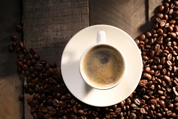 Cup of coffee with grains on wooden table, top view — Stock Photo, Image