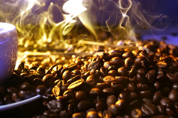 Pilha de grãos de café e xícara de café quente em feixe no fundo escuro — Fotografia de Stock