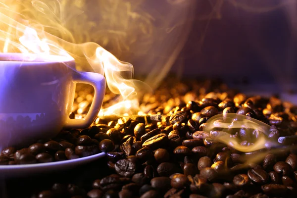 Pile de grains de café et tasse de café chaud dans le faisceau sur fond sombre — Photo