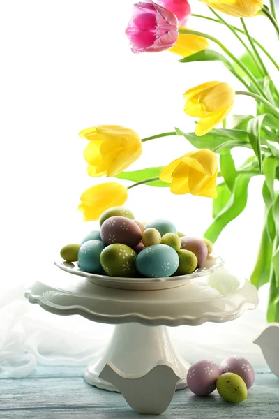 Huevos de Pascua en jarrón y tulipanes en mesa sobre fondo brillante —  Fotos de Stock