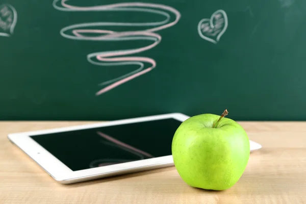 Tablet digital e maçã na mesa na frente do quadro-negro — Fotografia de Stock