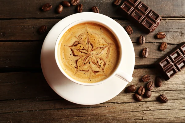 Xícara de café arte latte com grãos e chocolate na mesa de madeira, vista superior — Fotografia de Stock