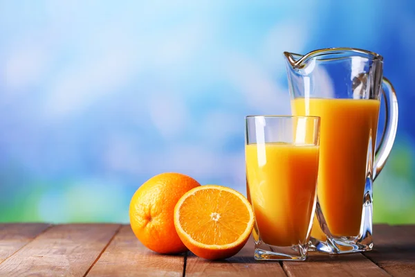 Vidro e jarro de suco de laranja na mesa de madeira no fundo natural — Fotografia de Stock