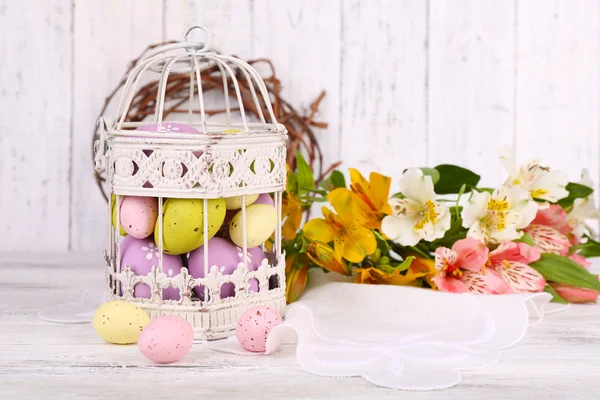 Composición de Pascua con huevos de Pascua en jaula decorativa y flores, sobre fondo de madera de color — Foto de Stock