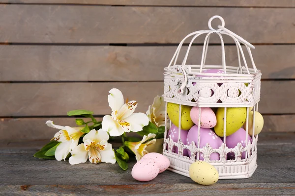Compoziția de Paști cu ouă de Paști în cușcă decorativă și flori, pe fundal din lemn — Fotografie, imagine de stoc