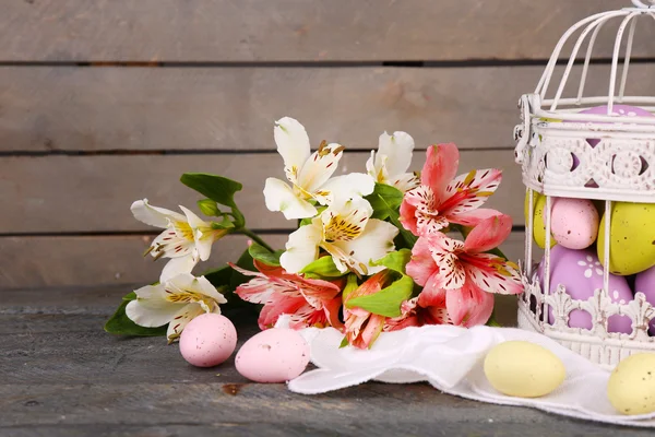 Composizione pasquale con uova di Pasqua in gabbia decorativa e fiori, su sfondo ligneo — Foto Stock