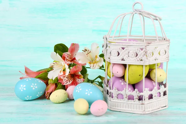 Ostern Komposition mit Ostereiern in dekorativem Käfig und Blumen, auf farbigem Holzhintergrund — Stockfoto