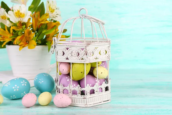 Composição de Páscoa com ovos de Páscoa em gaiola decorativa e flores, na cor de fundo de madeira — Fotografia de Stock